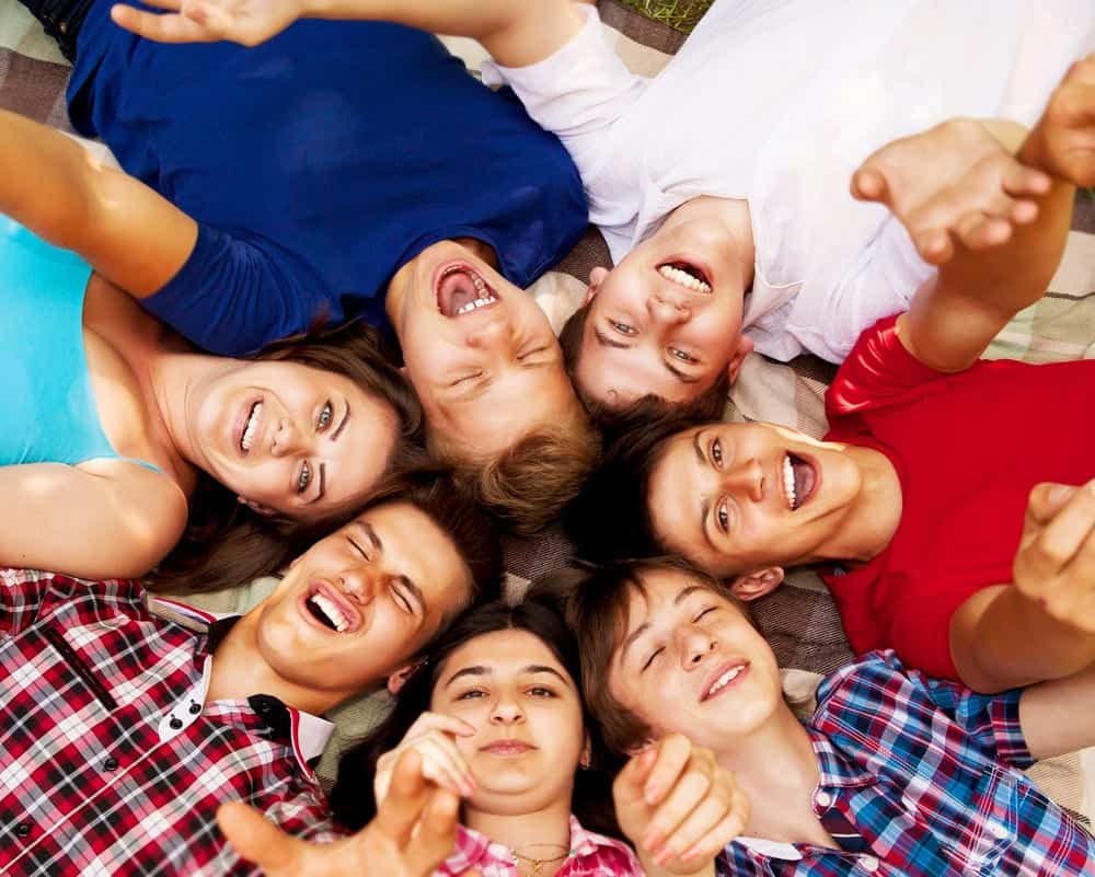 7 young adults laying on the ground in a circle and smiling up at the camera